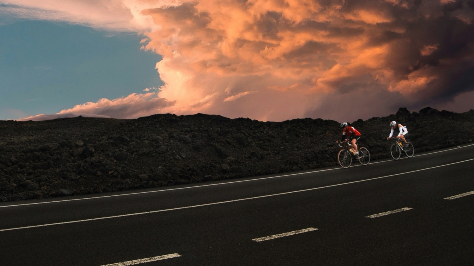 Two cyclists riding under a warm evening sky